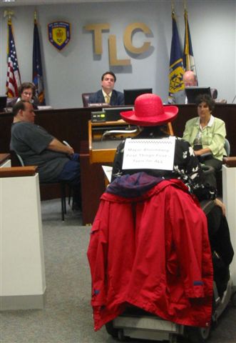 larger photo of far view of Jean Ryan speaking at a podium at TLC hearing