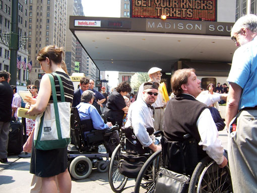 larger photo of people in wheelchairs talking to reporters in front of Madison Square Garden