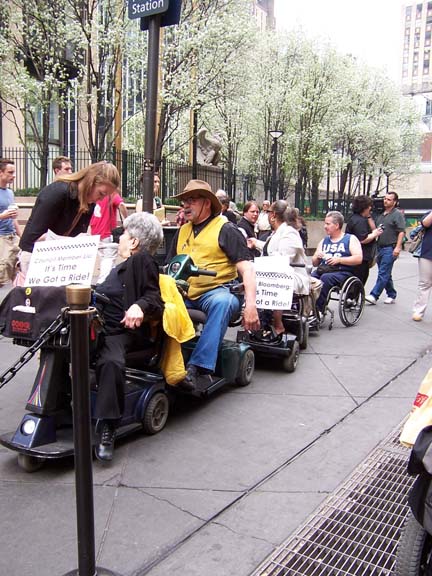 larger photo of people in wheelchairs and electric scooters at Penn Station taxi stand