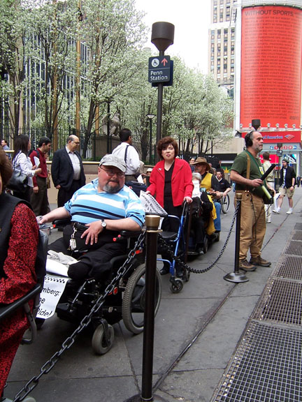 larger photo of people in wheelchairs and others using walkers at Penn Station taxi stand