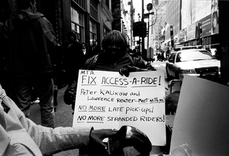 Pamela Bates holds sign reading Fix Access-A-Ride!