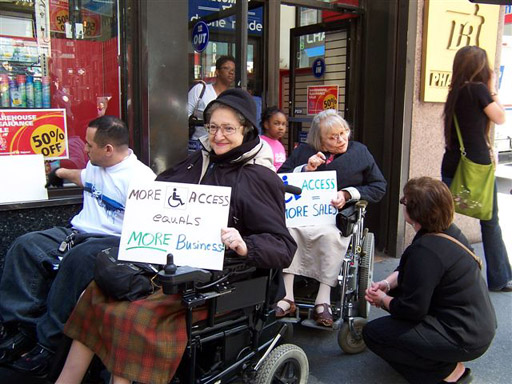 larger photo of a female activist in a wheelchair holding a sign reading More Access Equals More Business