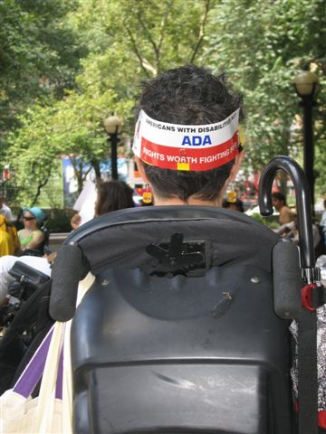 A person wears a sign on the back of her head that reads, "Americans with Disabilities Act ADA, Rights Worth Fighting For."