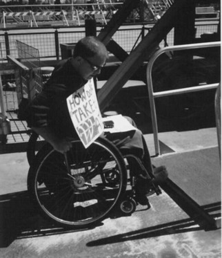 A man in a manual wheelchair encounters a step in his attempt to get to a ferry ramp.